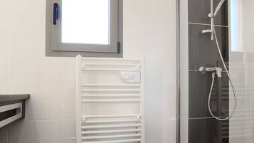 A modern bathroom with a glass shower enclosure, a white radiator, and a window above the radiator.