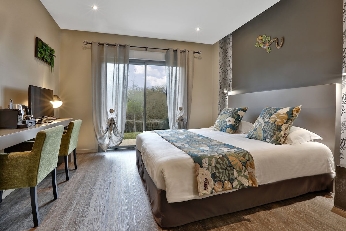 A bedroom with a large bed, a desk with a chair, and a window with curtains.