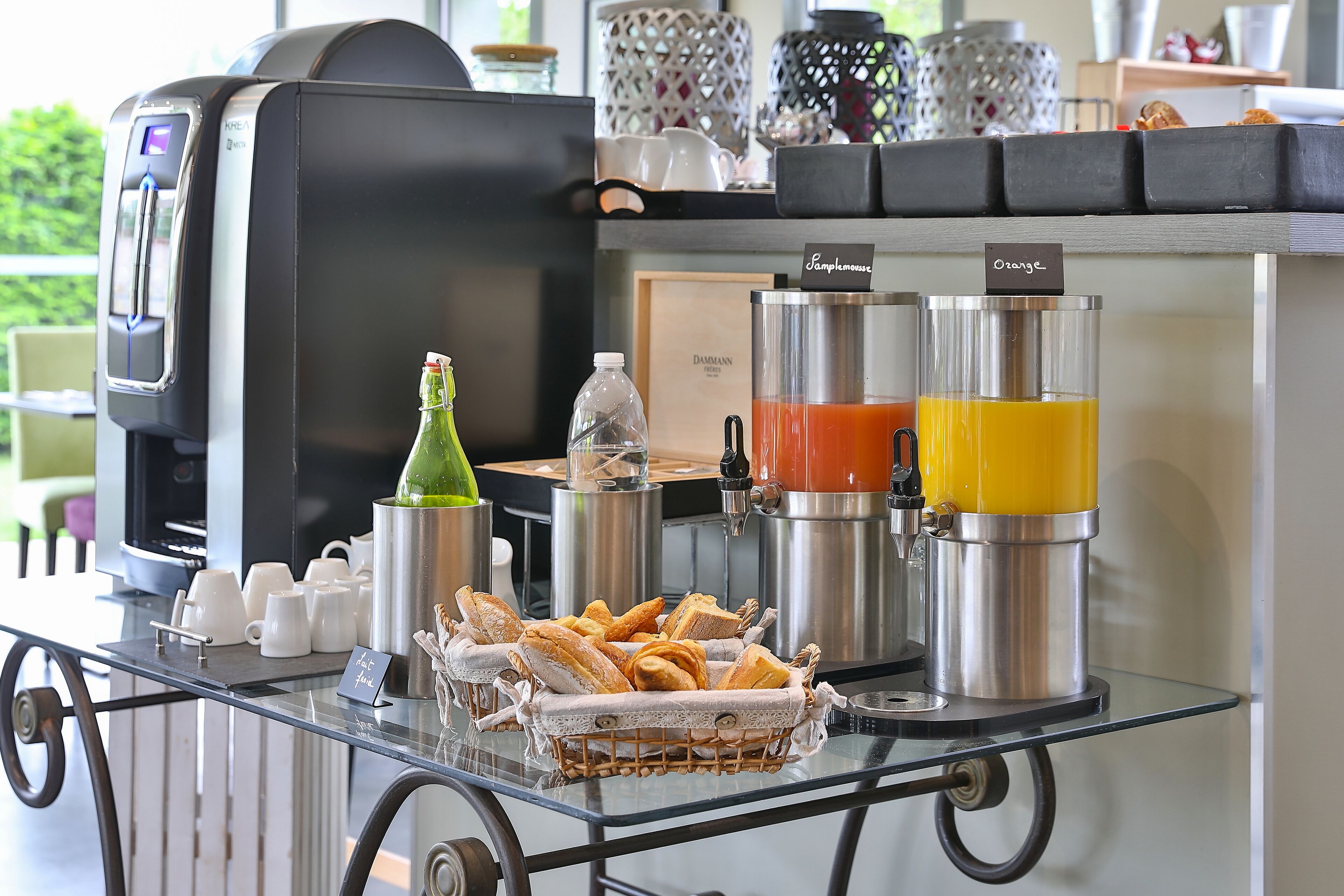 A breakfast bar with coffee machines, a juice dispenser, and a basket of croissants.