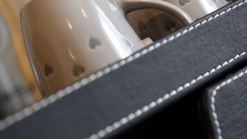 A close-up of a black leather bag with white stitching, containing two white mugs with heart designs.