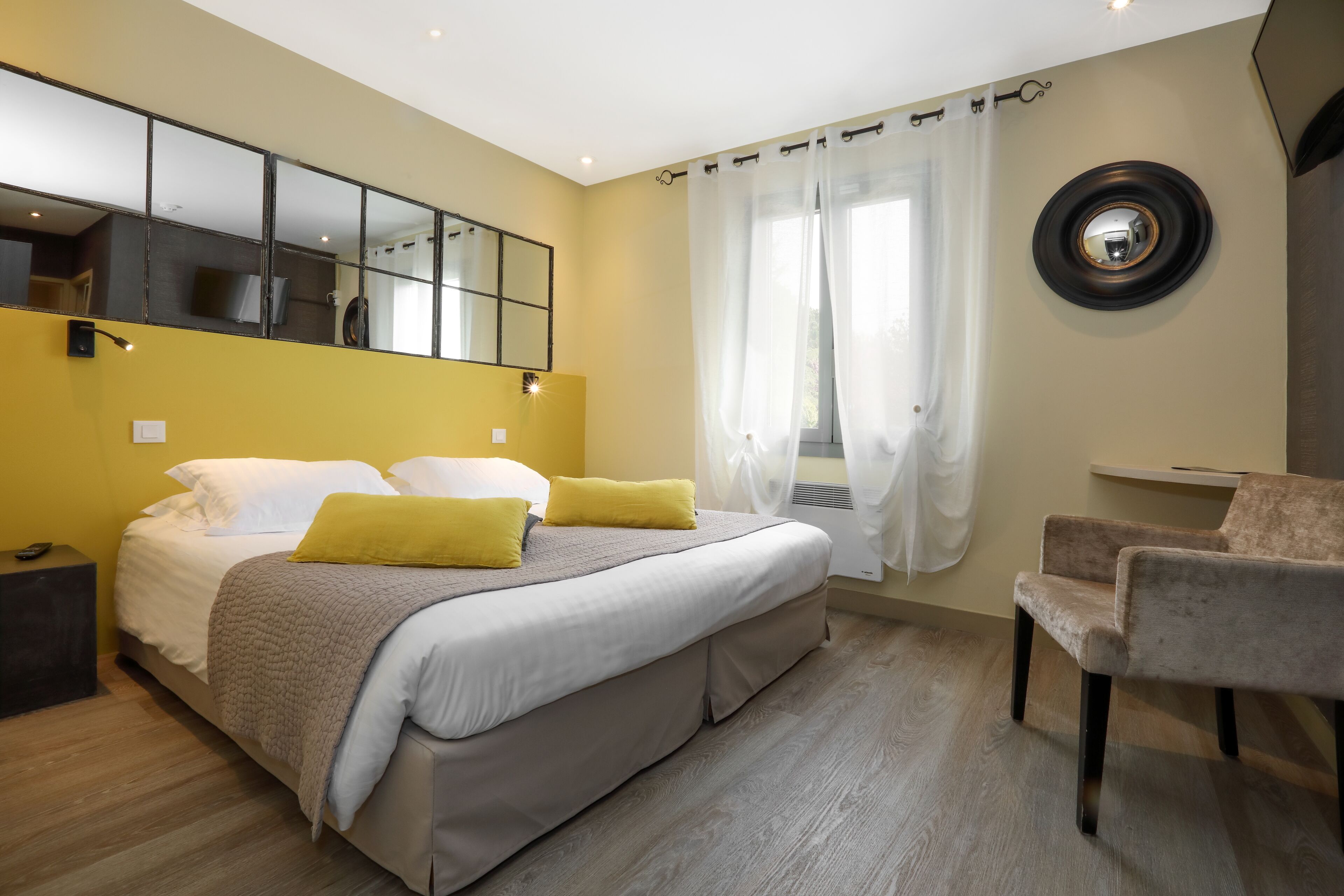 Un dormitorio con cama, mesita de noche, silla y espejo en la pared.