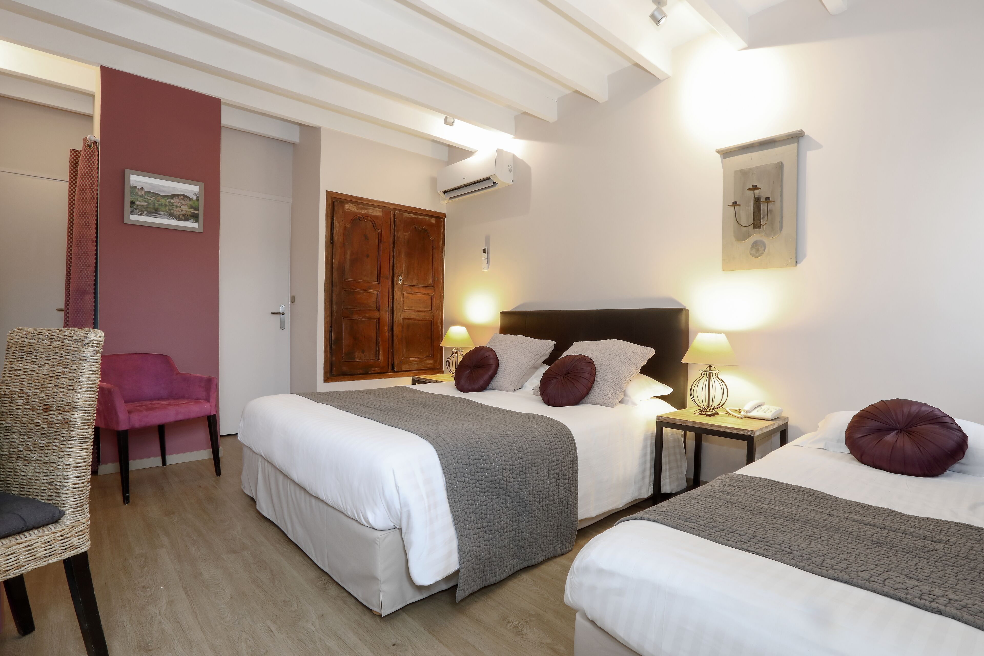 Una camera d'albergo con due letti, un armadio in legno, una sedia e un comodino con una lampada.