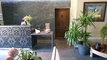 Un área de recepción con un mostrador estampado, una puerta de madera y diversas plantas en macetas.