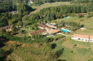 An aerial view of a residential area with multiple houses, a swimming pool, and a large green field. - Le Mas de Castel (Sarlat-la-Canéda)