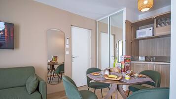 A modern living room with a sofa, dining table, chairs, a kitchen area with a microwave, and a hanging light fixture.