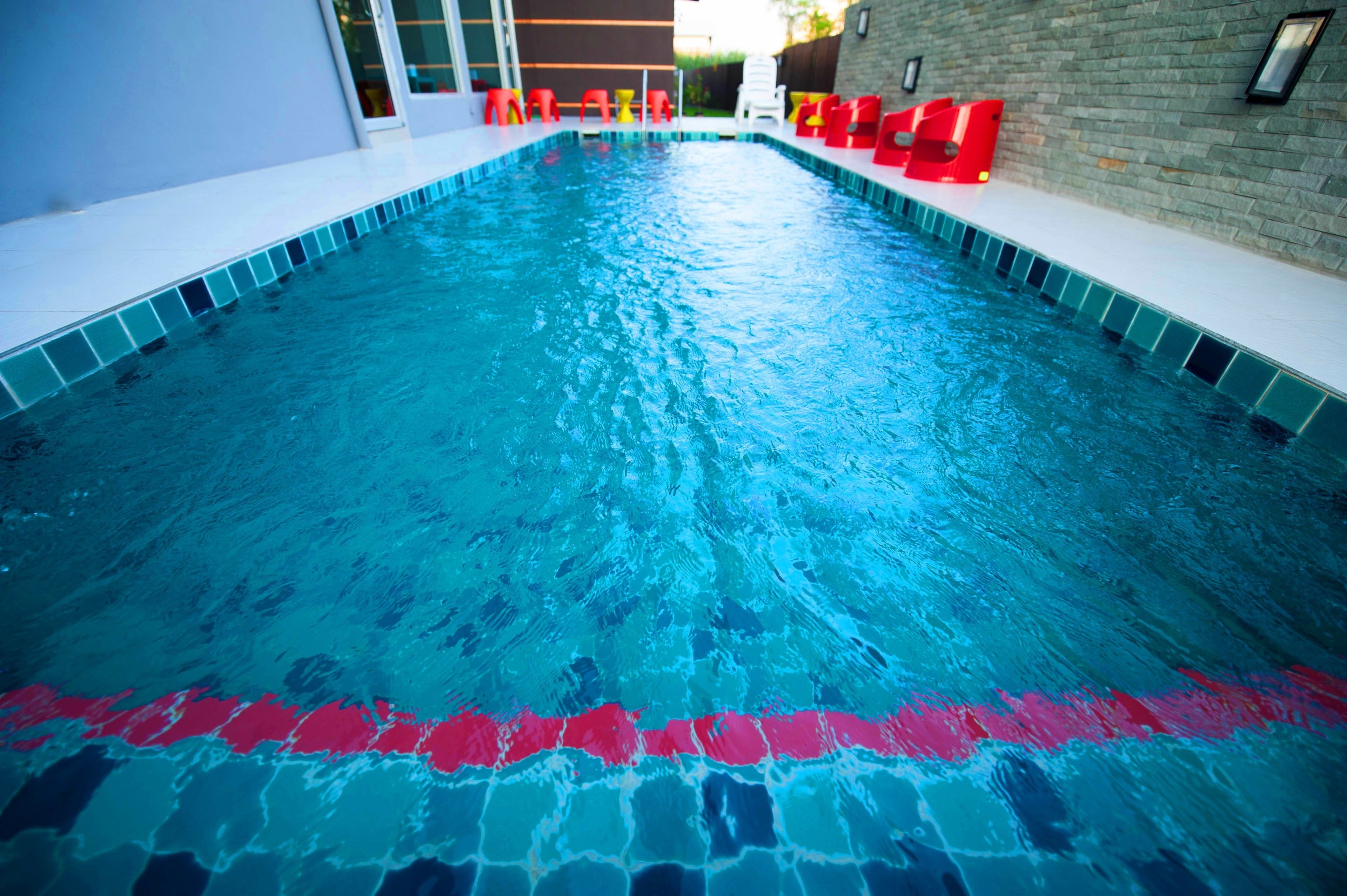 A swimming pool with clear blue water, tiled edges, and red poolside chairs.