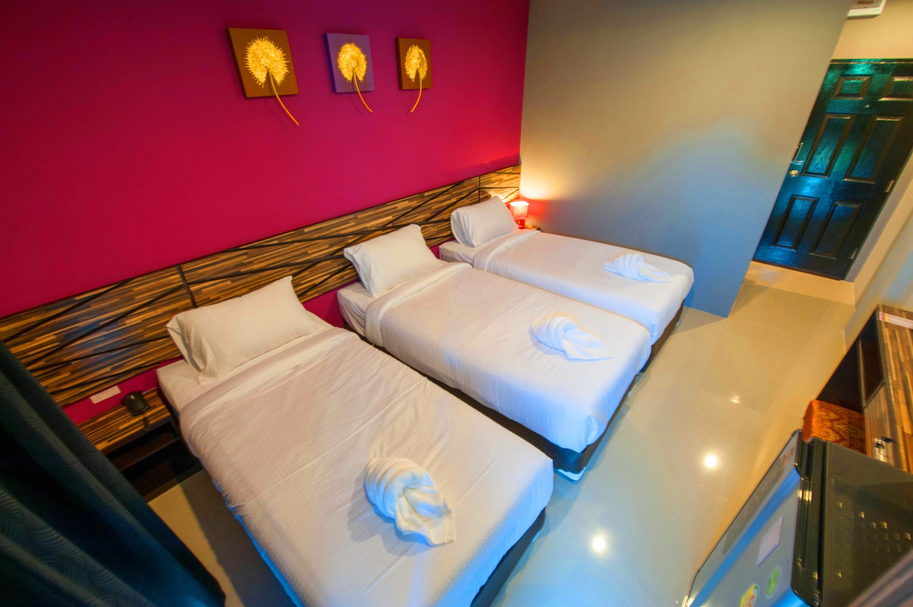 A hotel room with two beds, a wooden headboard, a red accent wall, and a small table with a lamp.