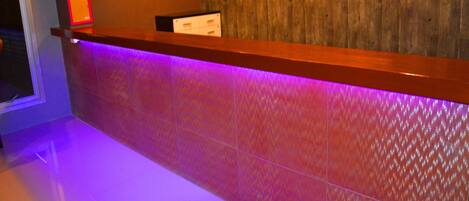 A reception area with a wooden wall, a 'dwella' sign, a flat-screen TV, and a purple-lit reception desk.