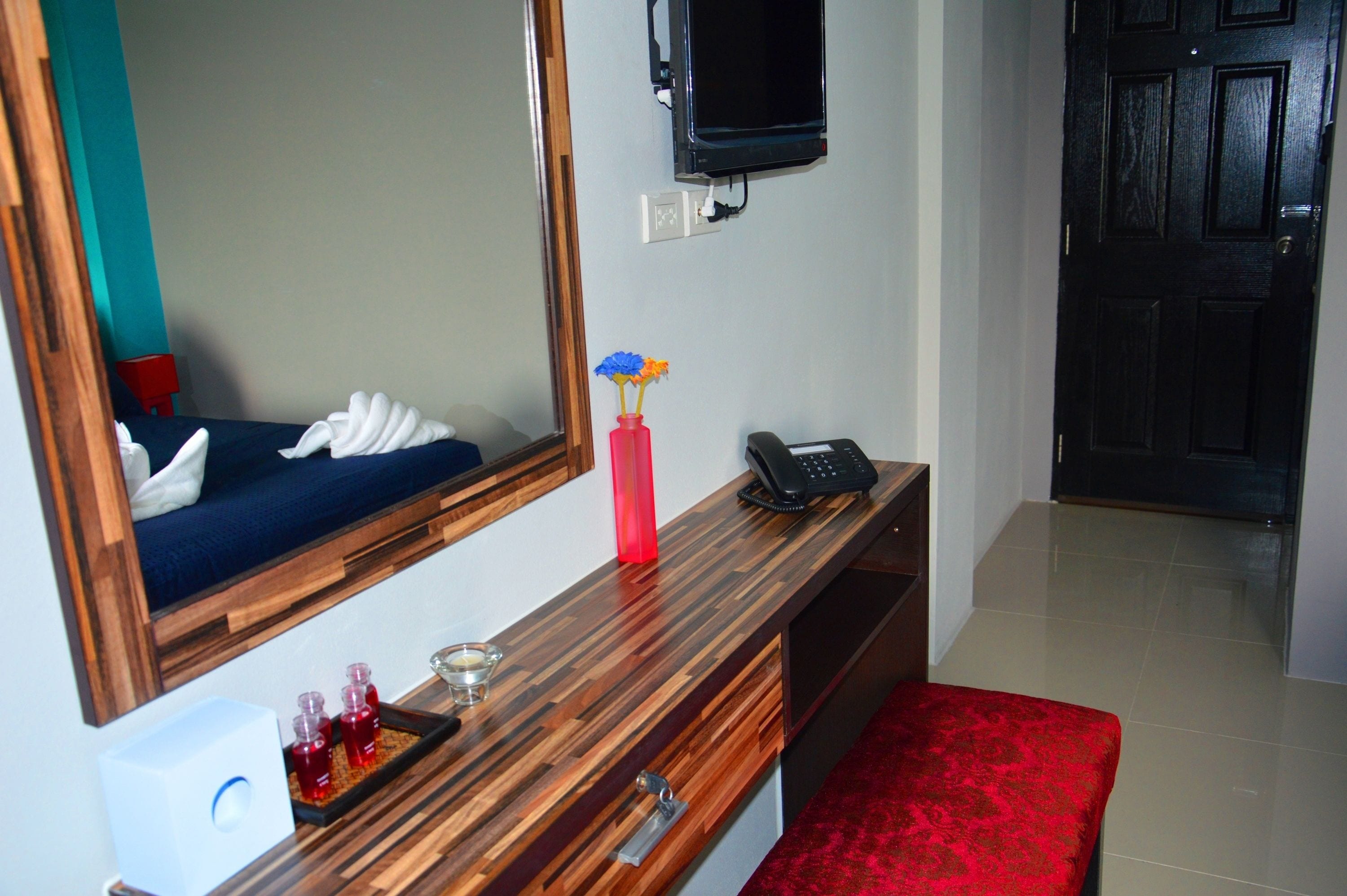 A hotel room with a wooden desk, a red vase with flowers, a telephone, and a mirror.