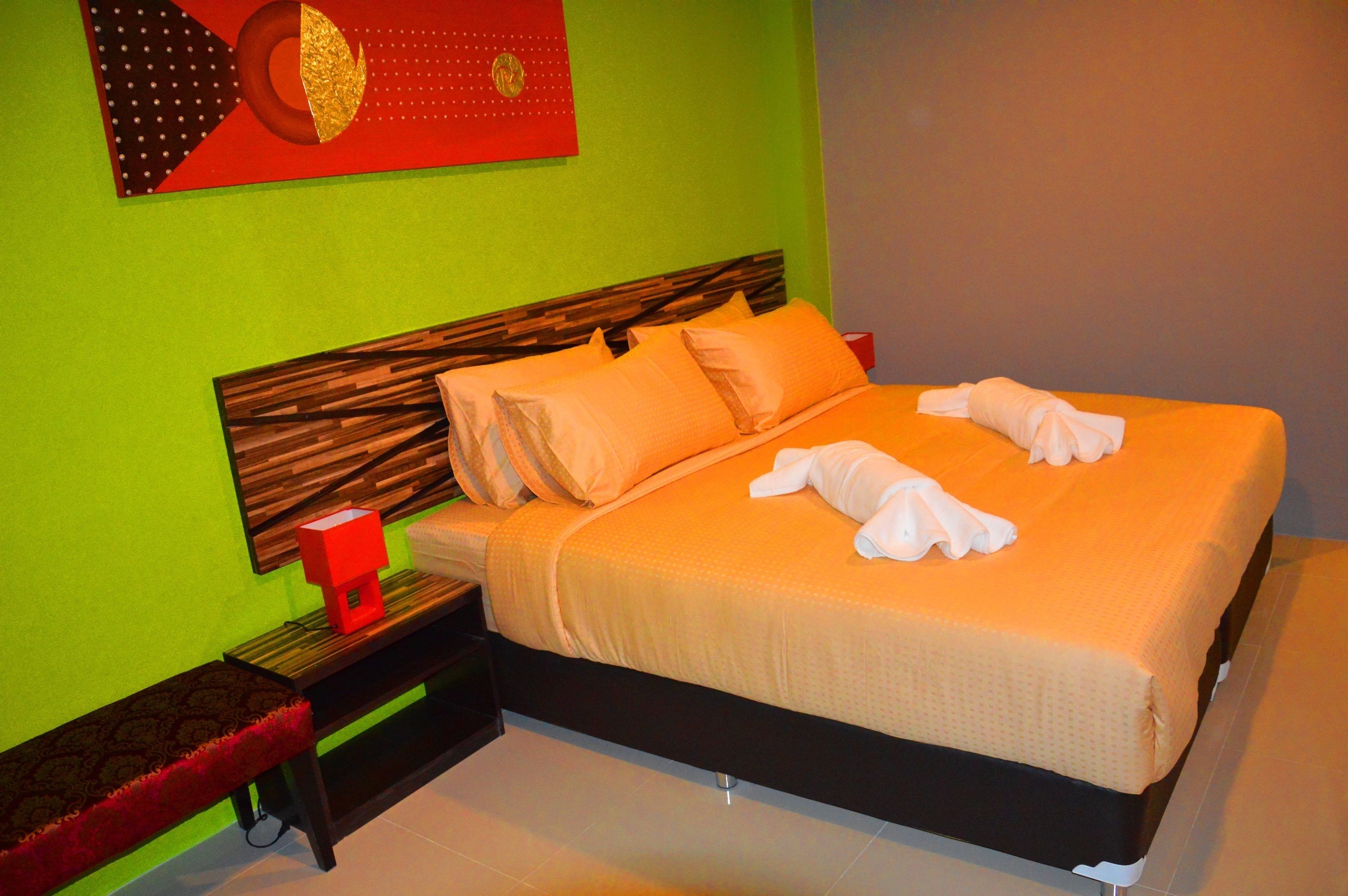 A neatly made bed with orange bedding, a wooden headboard, and a red bedside table with a lamp.