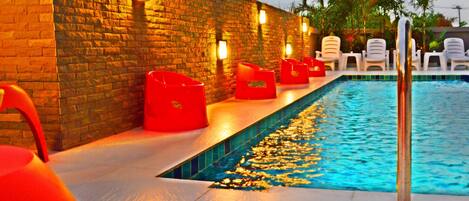 A poolside area with a brick wall, red chairs, and a pool.