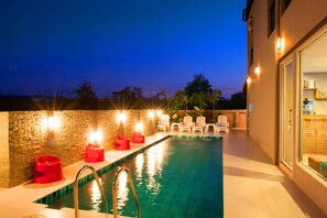 A swimming pool with a brick wall, a metal ladder, and several red and white lounge chairs. - Dwella Suvarnabhumi (Bang Phli)