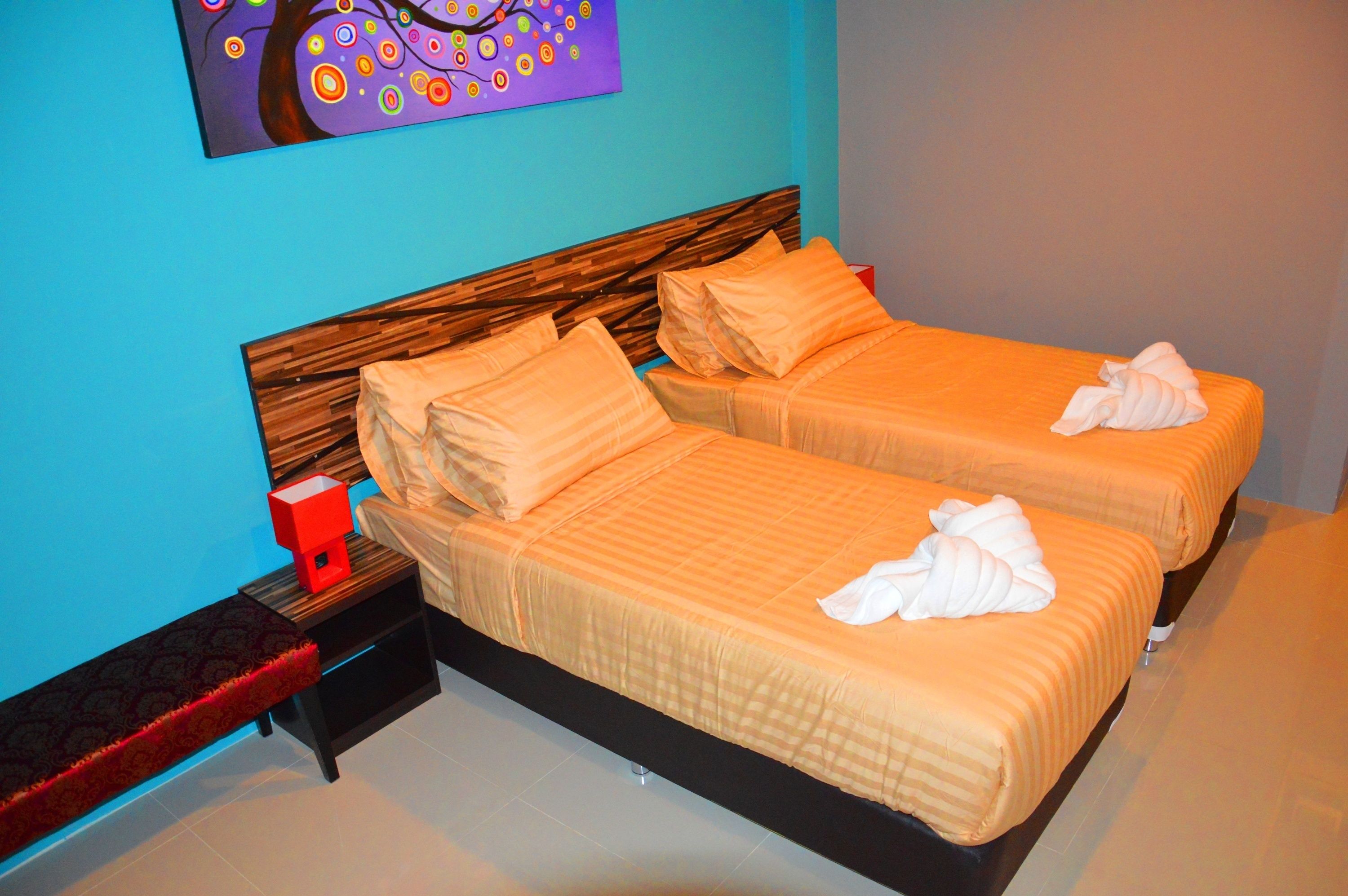 Quarto de hotel com duas camas, uma mesa de cabeceira, uma caixa vermelha e um quadro na parede.