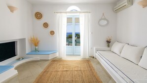 Una sala de estar moderna con un sofá, un televisor, un amplio ventanal con cortinas y vista al mar.