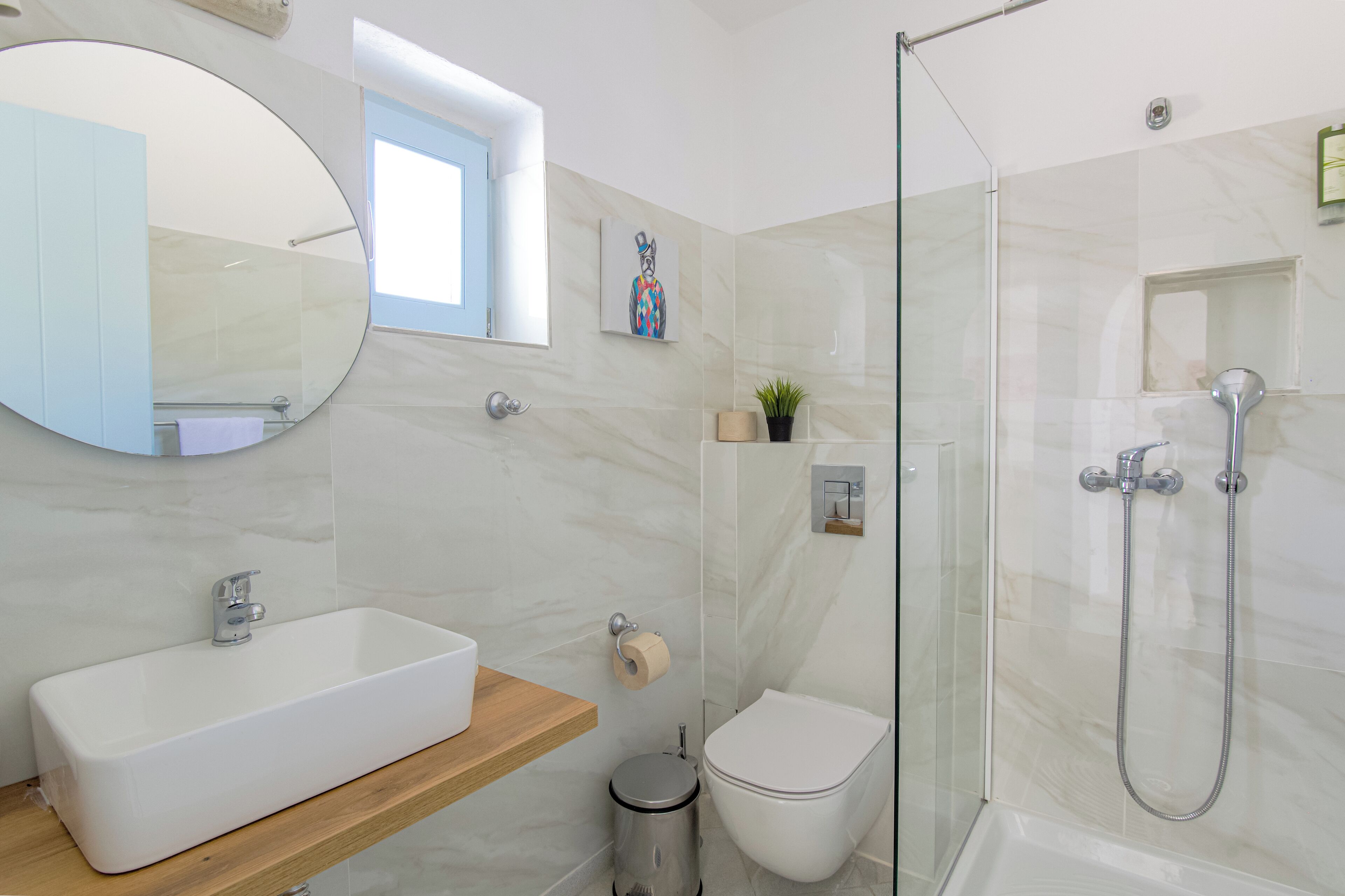 Une salle de bain moderne avec un grand miroir ovale, un lavabo rectangulaire, des toilettes et une cabine de douche en verre.
