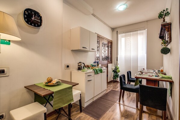 A compact kitchen with a dining area, a clock, and a small table with a green tablecloth.