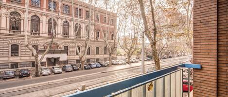 A view of a street with parked cars and a building with arched windows and a balcony.