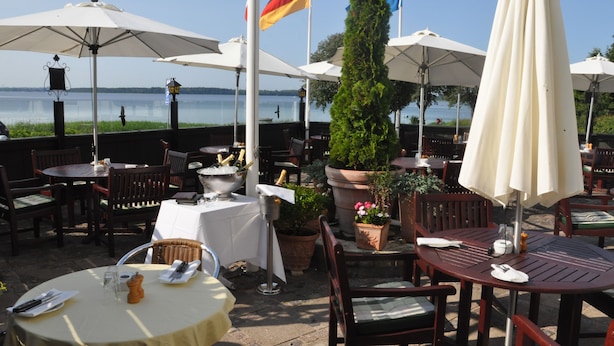 An outdoor dining area with tables and chairs, umbrellas, and flags. - Hotel Fjordkroen (Tappernoje)