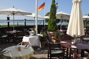 An outdoor dining area with tables and chairs, umbrellas, and flags. - Hotel Fjordkroen (Tappernoje)