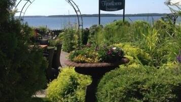 Un espace aménagé en jardin, avec une enseigne indiquant «
Le Restaurant du Jardin aux Parfums
» et une vue sur l’eau en arrière-plan.