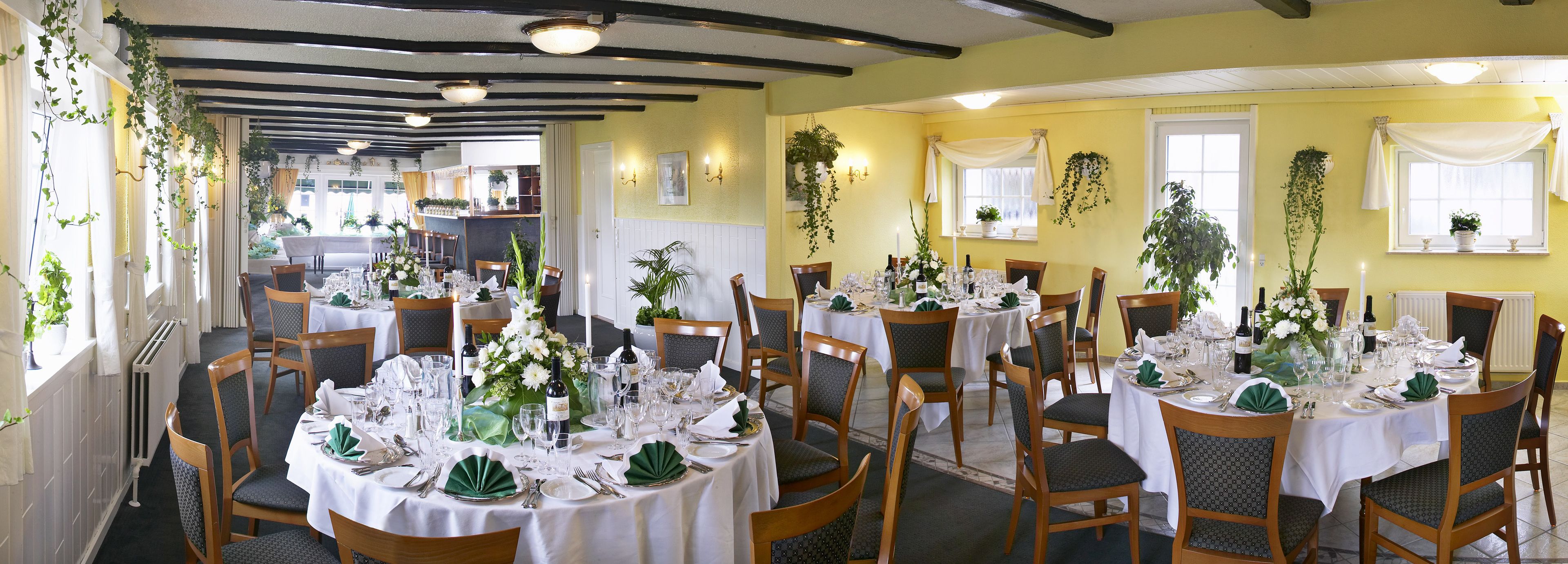 A restaurant with multiple round tables set for dining, featuring white tablecloths and green napkins.