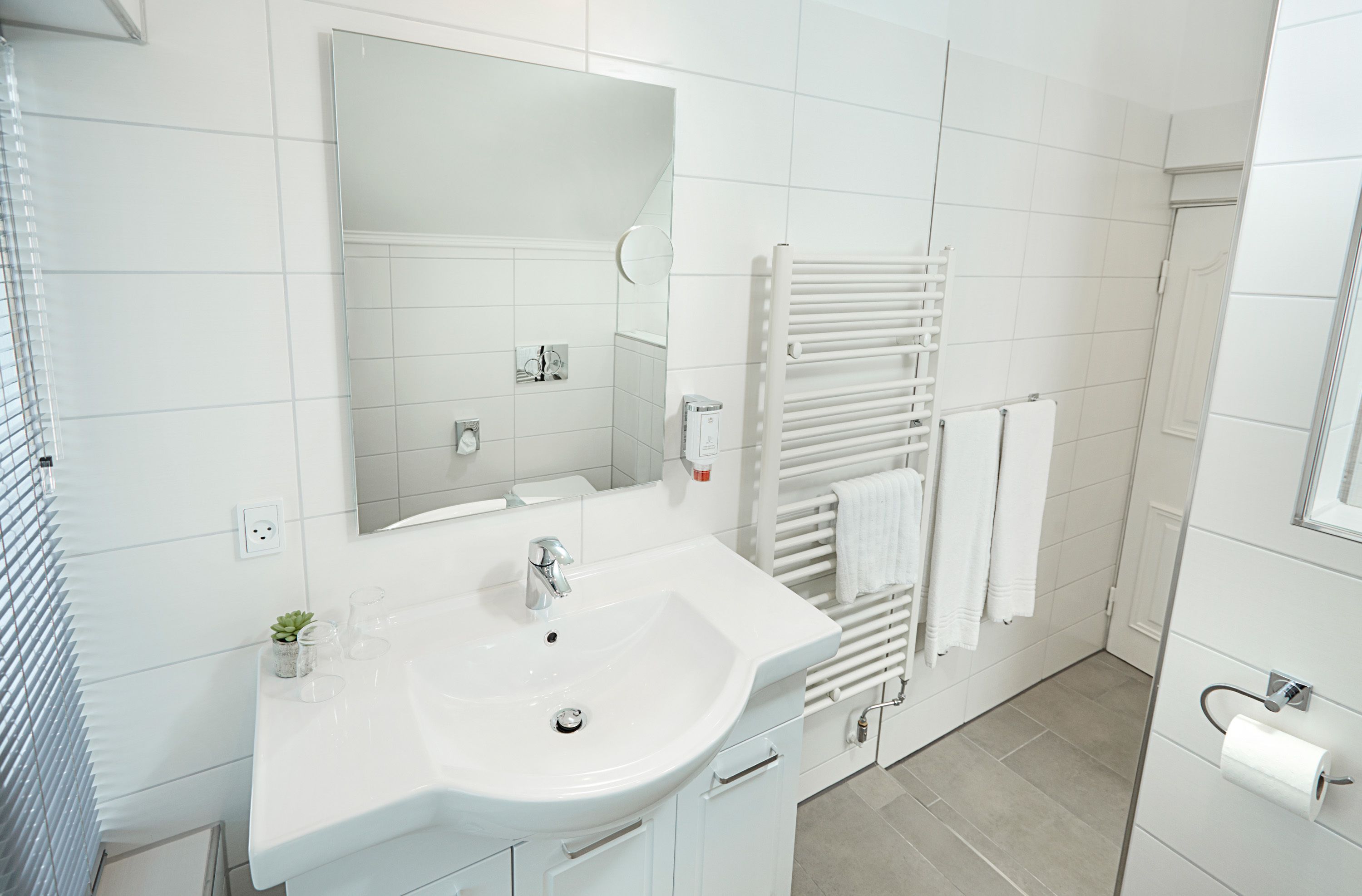 A modern bathroom with a white sink, mirror, and towel rack.