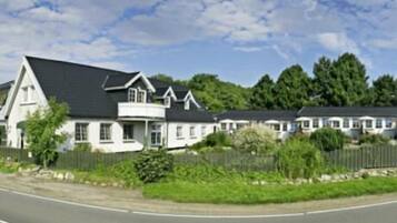 A row of white houses with dark roofs, surrounded by greenery and a clear sky.