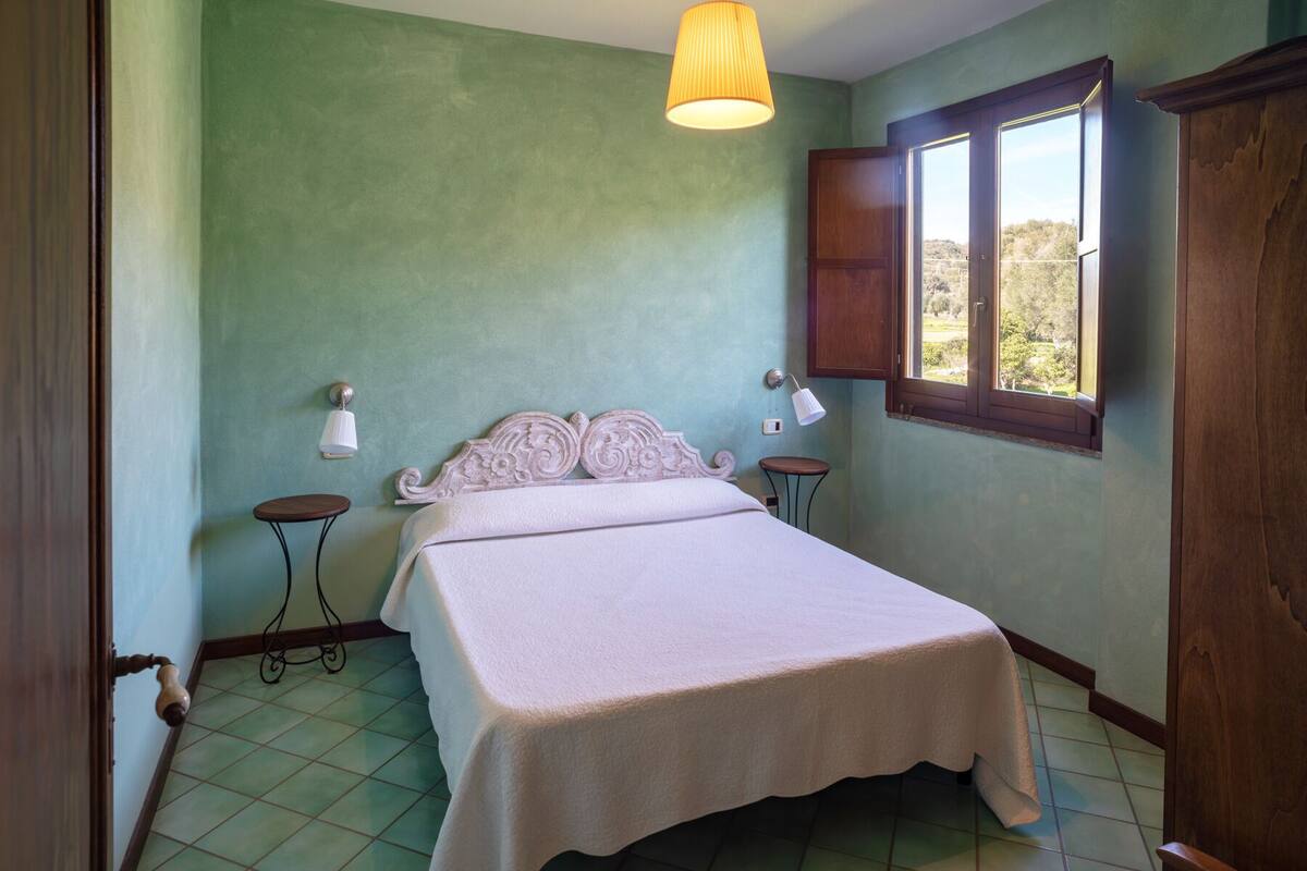 A bedroom with a bed, two bedside tables, a window, and a door.