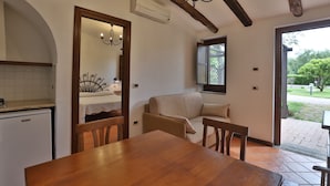 A cozy kitchen with a wooden table and chairs, a built-in oven, and a window overlooking a garden.