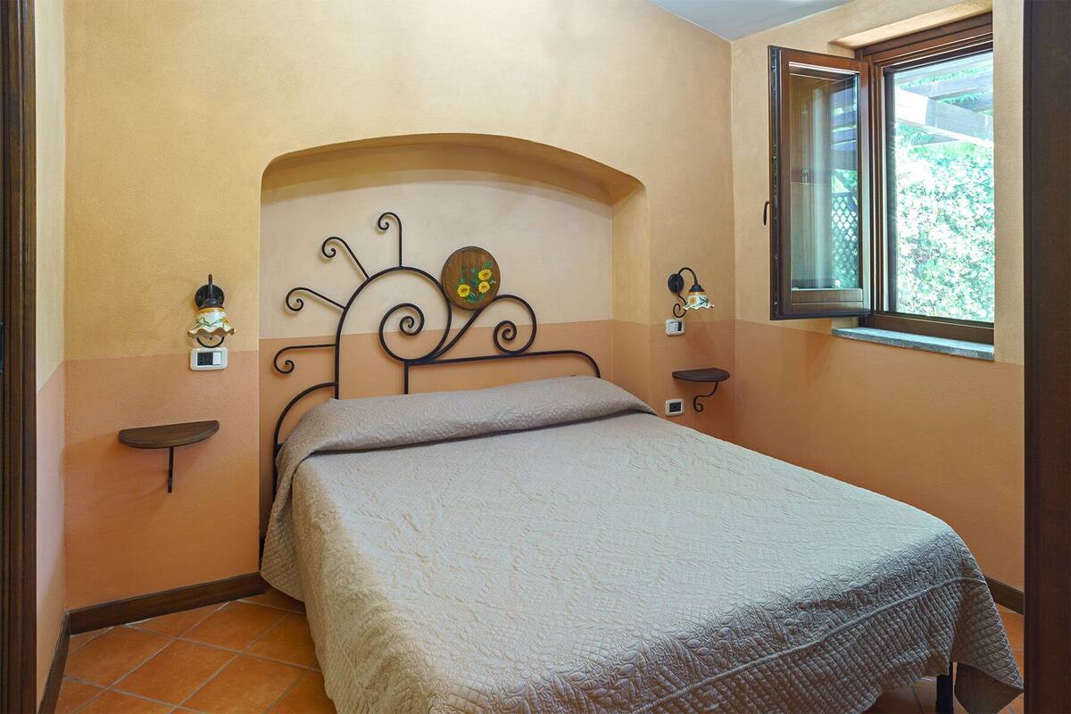 A bedroom with a bed, a window, and two wall-mounted lamps.