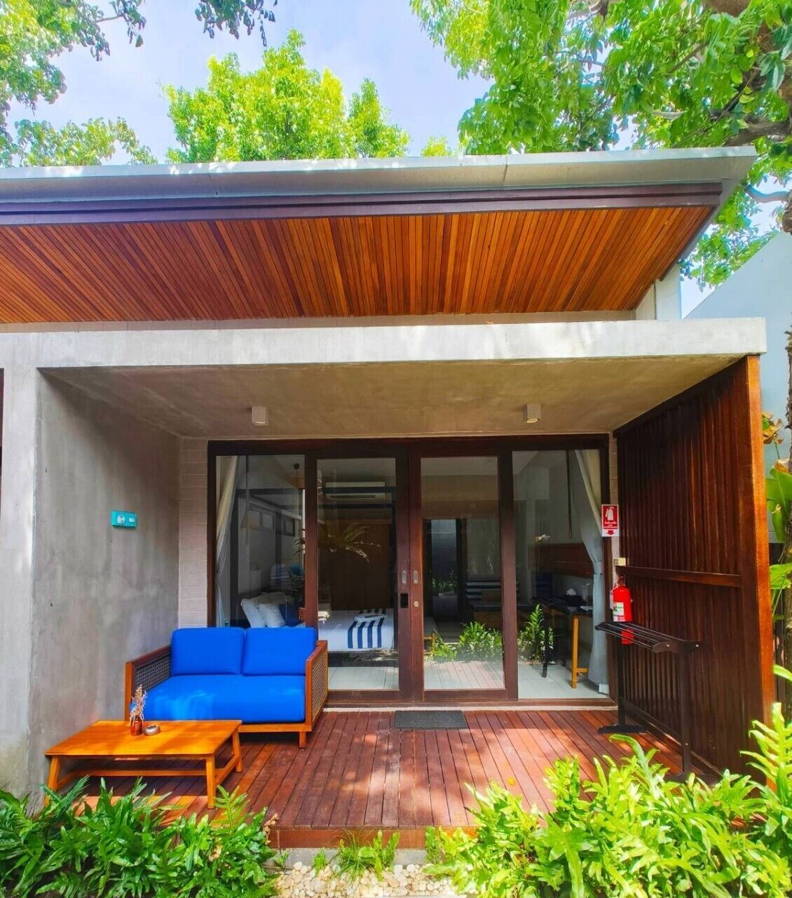 A modern house with a wooden deck, a blue sofa, and a glass door leading to a living area.