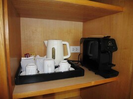 Uma área de cozinha com cafeteira, chaleira e vários copos brancos em um suporte.
