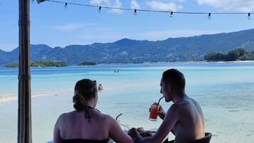 Dos personas cenando en una mesa al aire libre con vistas a una playa y montañas.