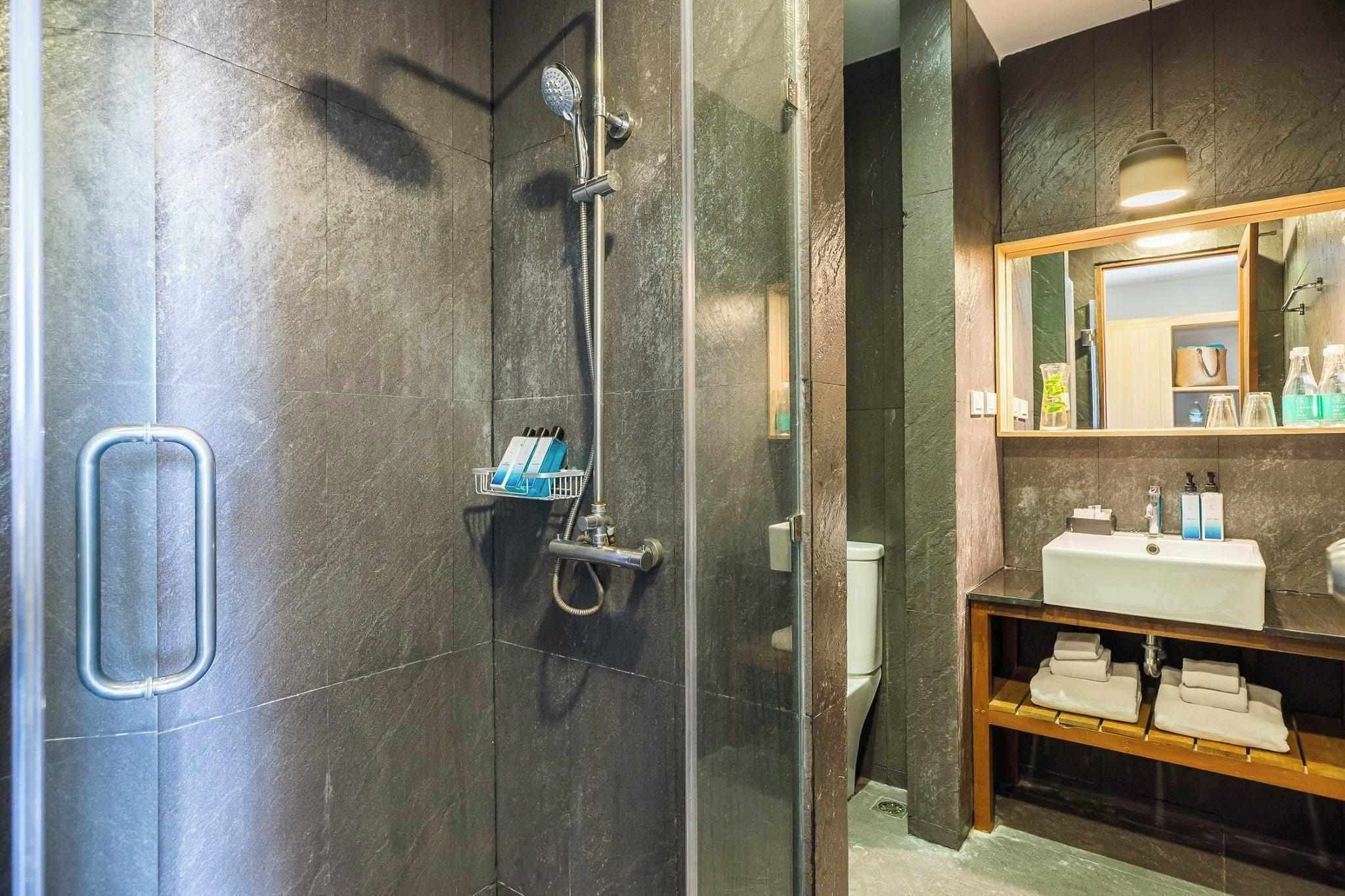 Un baño moderno con ducha de vidrio, tocador de madera con espejo y inodoro empotrado.