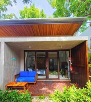 Una casa moderna con una terraza de madera, un sofá azul y una puerta de cristal que da a un patio.