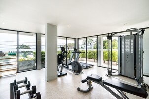 A modern gym with various exercise equipment, large windows, and a view of greenery outside.