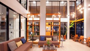 A modern lobby with a brown sofa, a coffee table, and wooden shelves with decorative items. - Casa De Mar (Koh Samui)