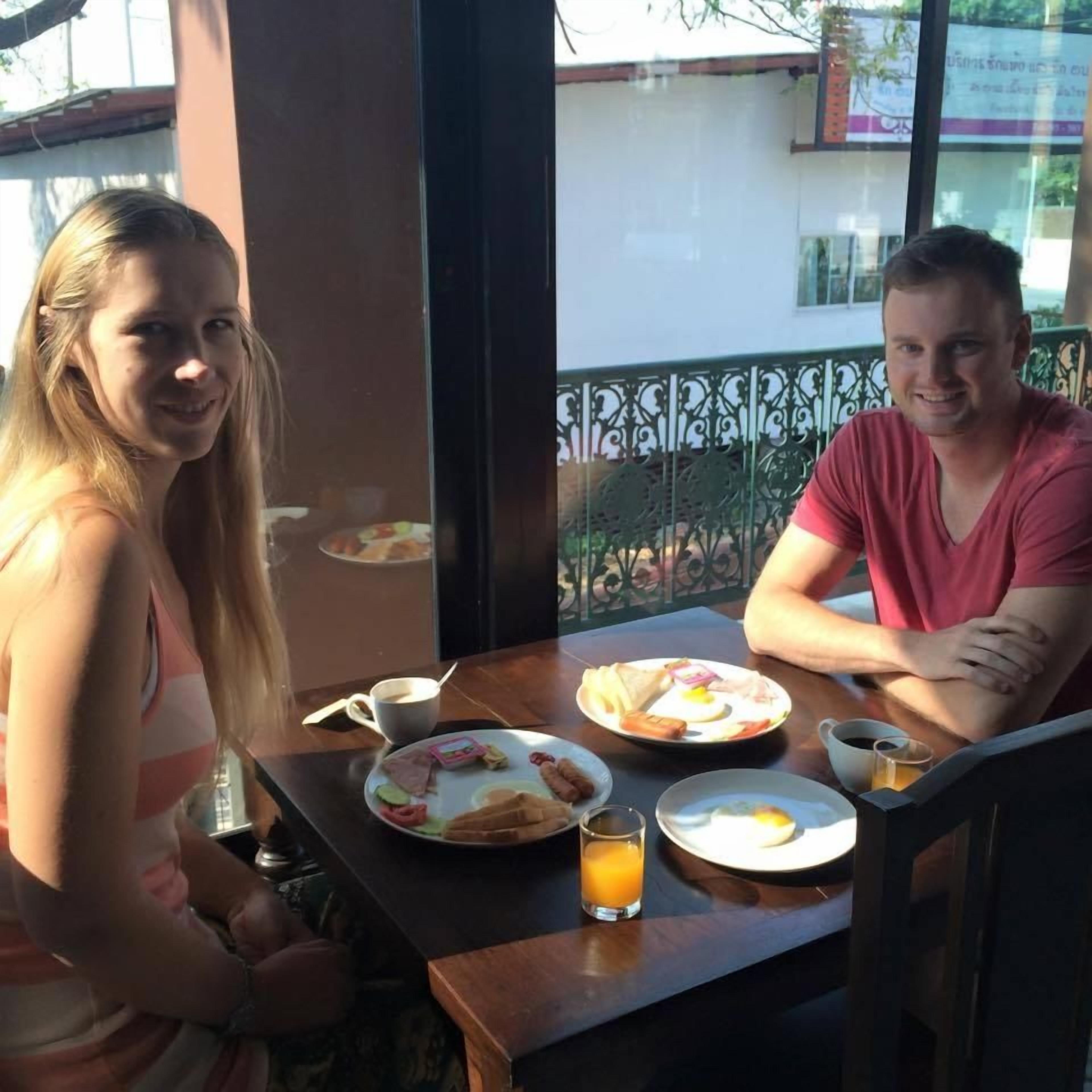 Deux personnes sont assises à une table, devant des assiettes de petit-déjeuner, un verre de jus d’orange et une tasse de café.
