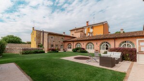 A courtyard with a lawn, outdoor furniture, and a building with a tiled roof and arched windows. - Residence Corte San Carlo (Lazise)