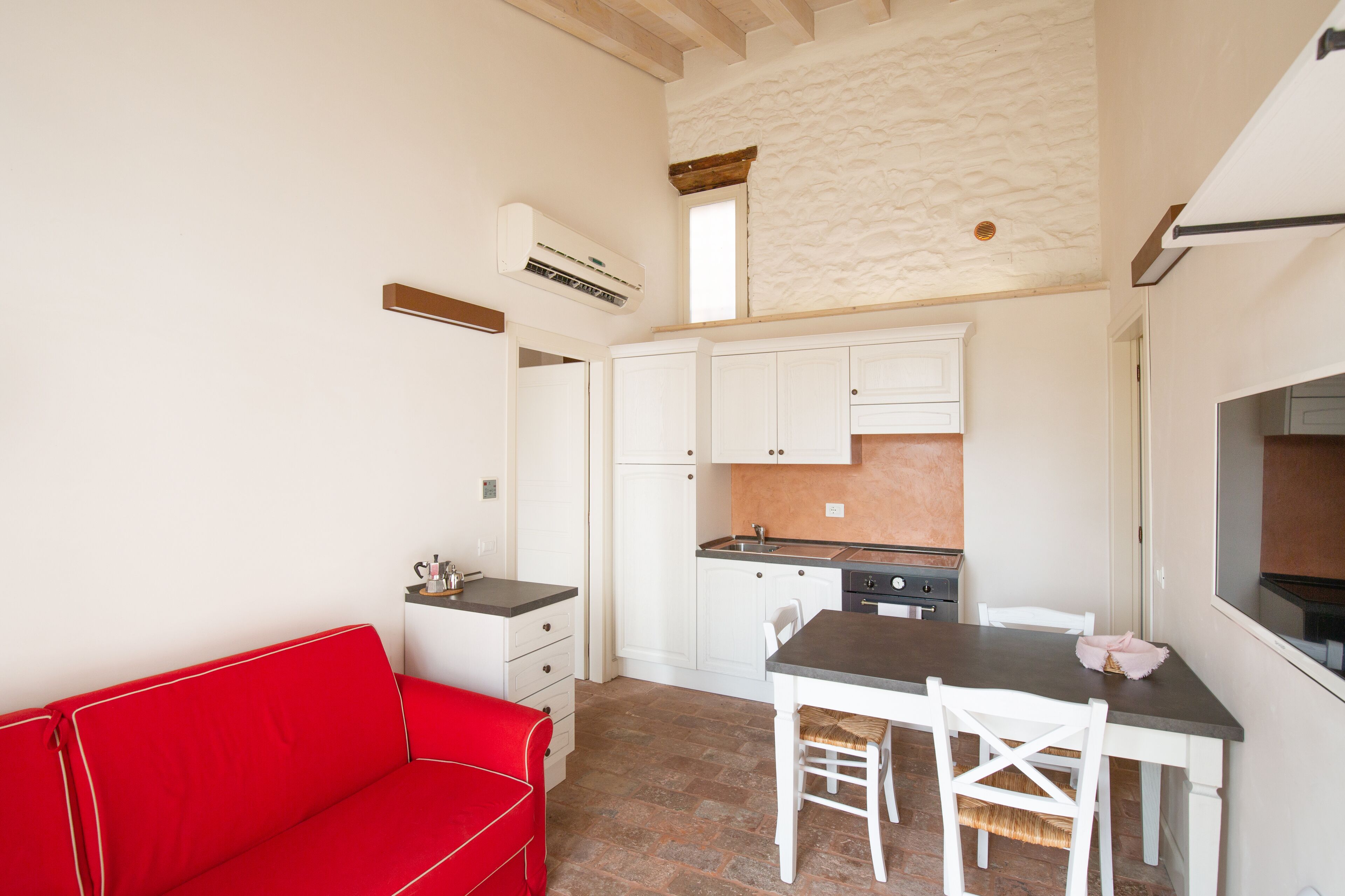 A compact kitchen with white cabinets, a red sofa, and a dining table with chairs.