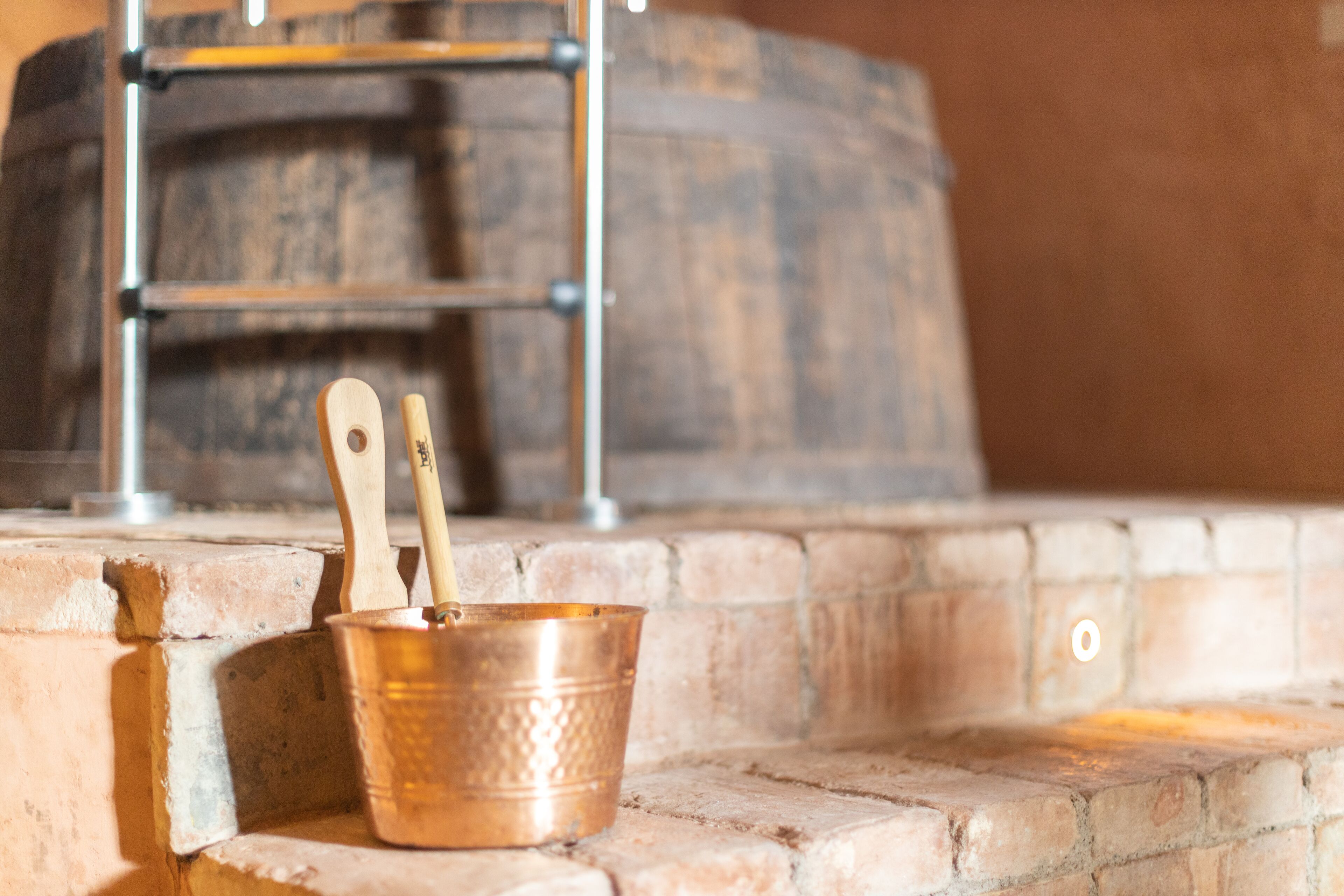 A copper bucket with wooden utensils on a brick ledge.