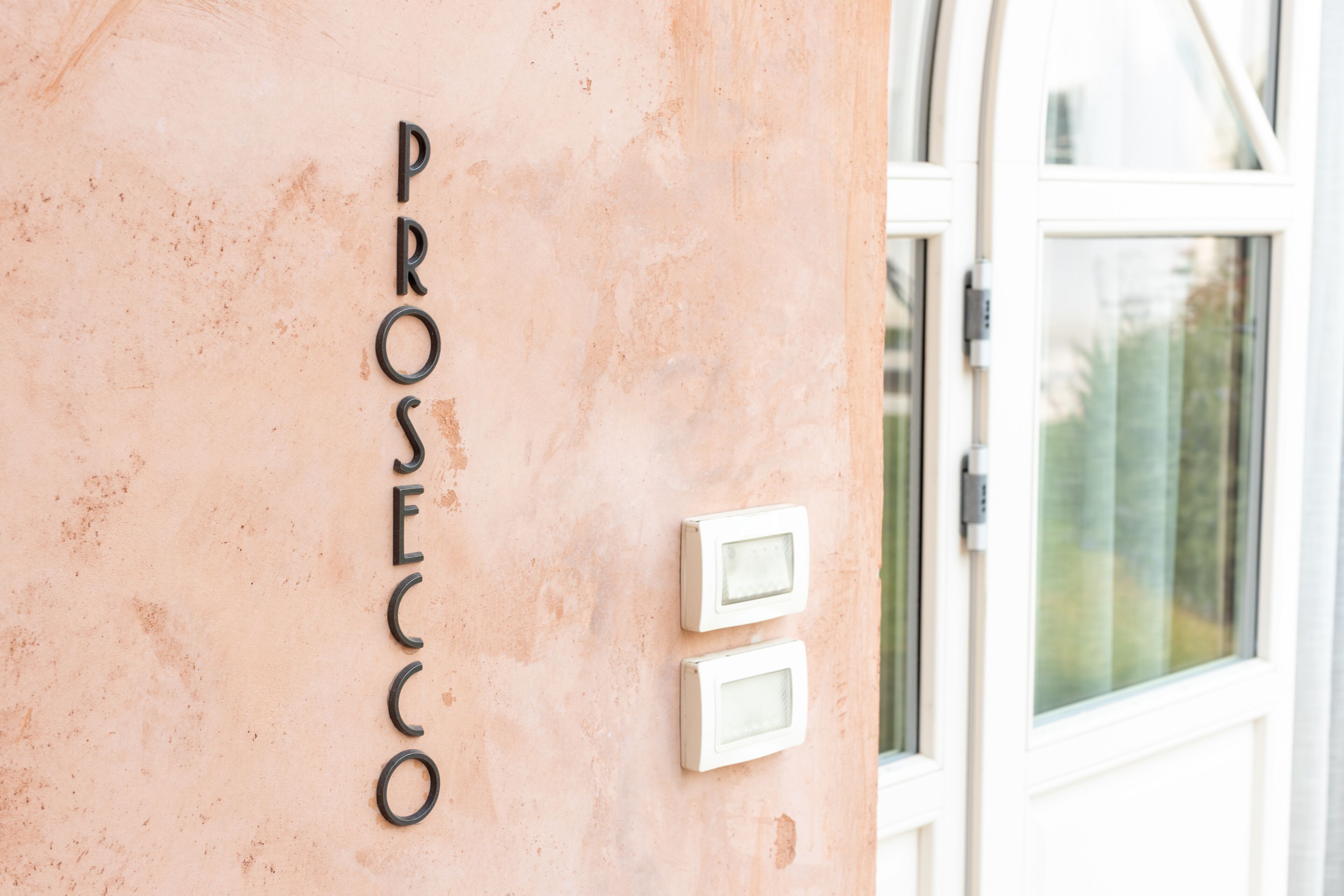 Fachada de un edificio con el nombre "PROSECCO" en una pared con textura.