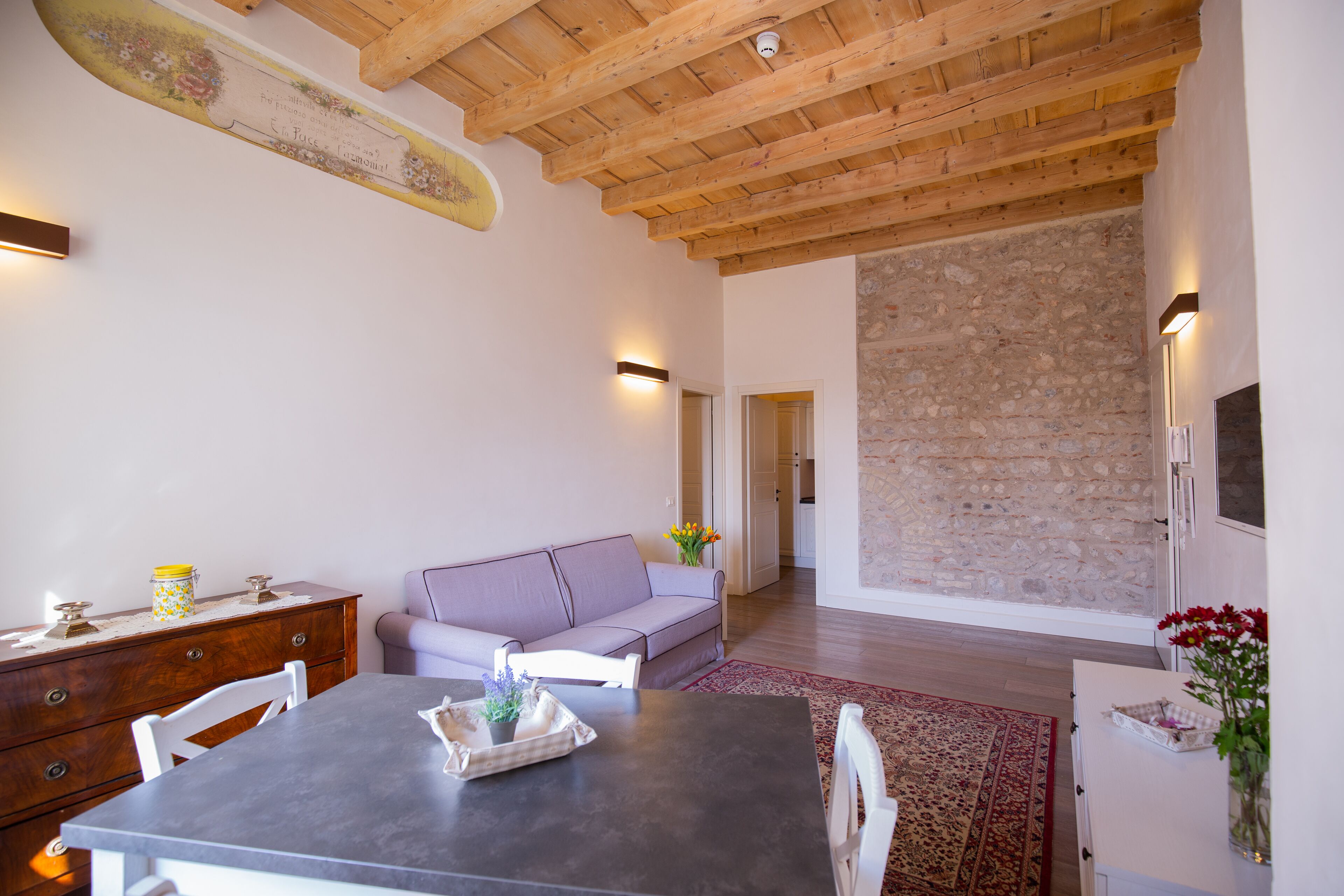Un vaste espace de vie doté d’un plafond en bois, d’un mur en pierre, d’un canapé, d’une table à manger et d’un coin cuisine.
