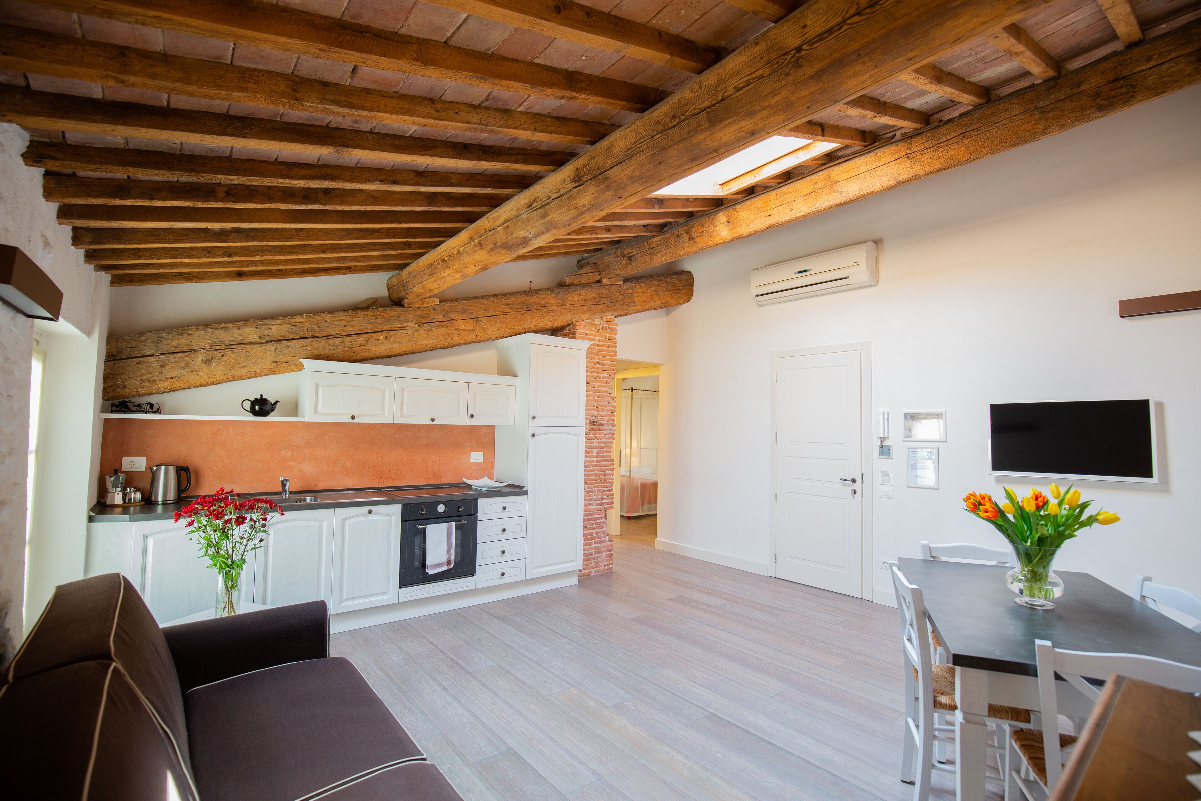 A modern kitchen with white cabinets, a brick wall, and a wooden ceiling.