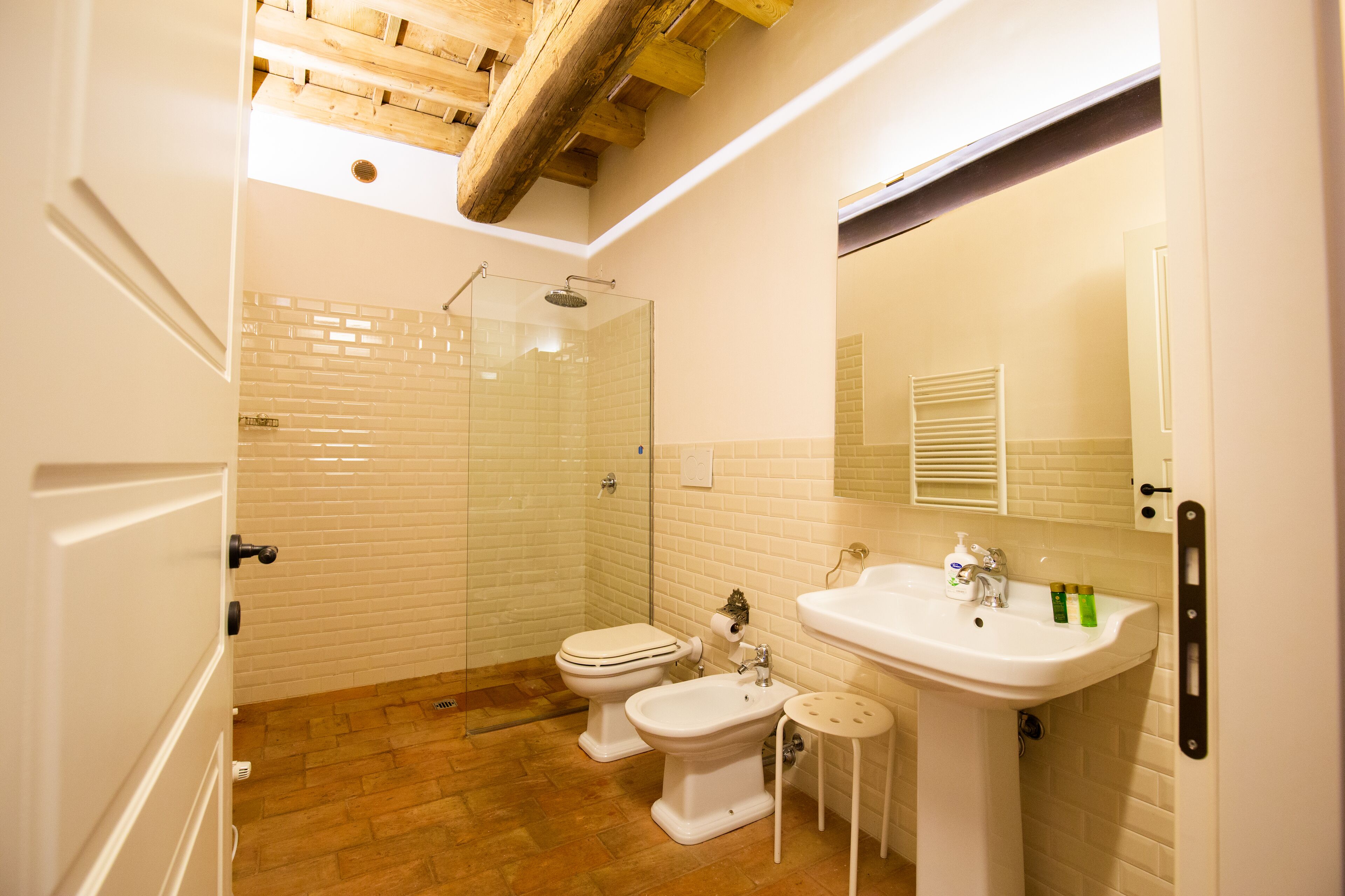 A bathroom with a glass-enclosed shower, a toilet, a bidet, and a sink with a mirror above it.