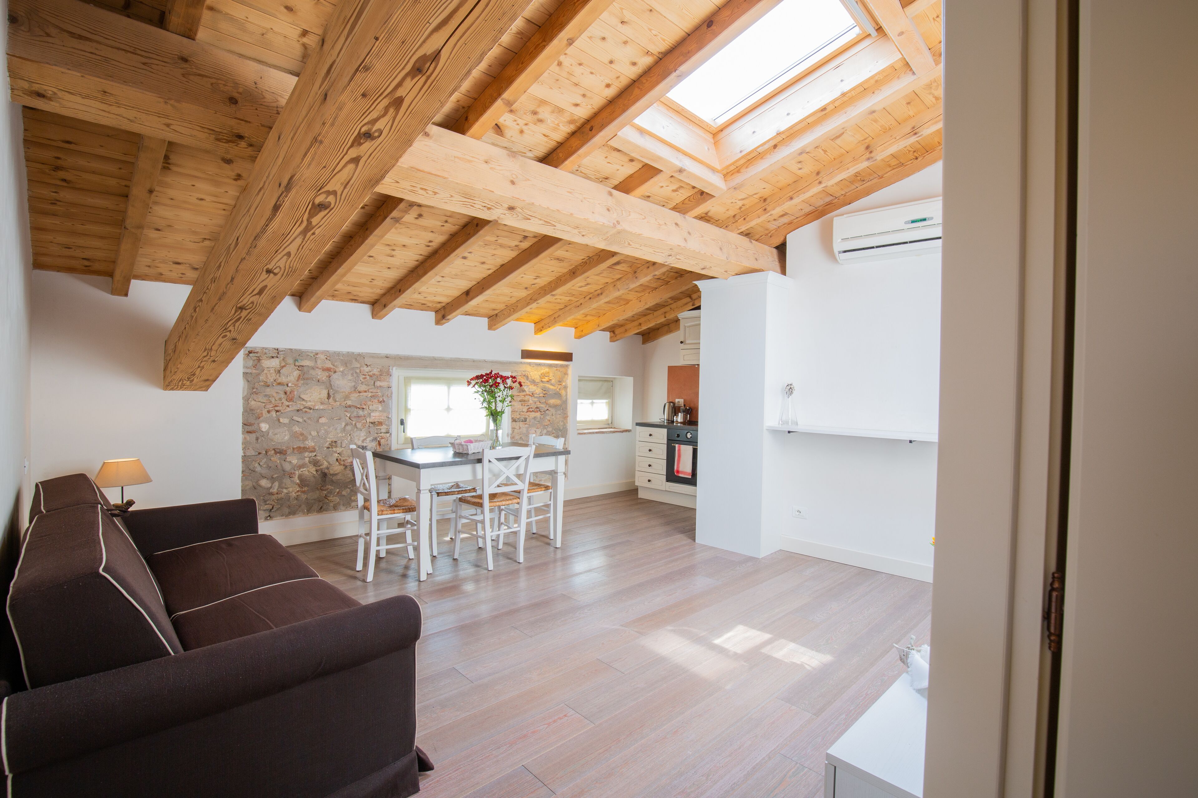 Amplia sala de estar con techo de madera, pared de piedra y cocina al fondo.