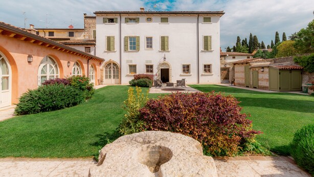 A two-story building with a central entrance, surrounded by a well-maintained lawn and a large rock in the foreground. - Residence Corte San Carlo (Lazise)