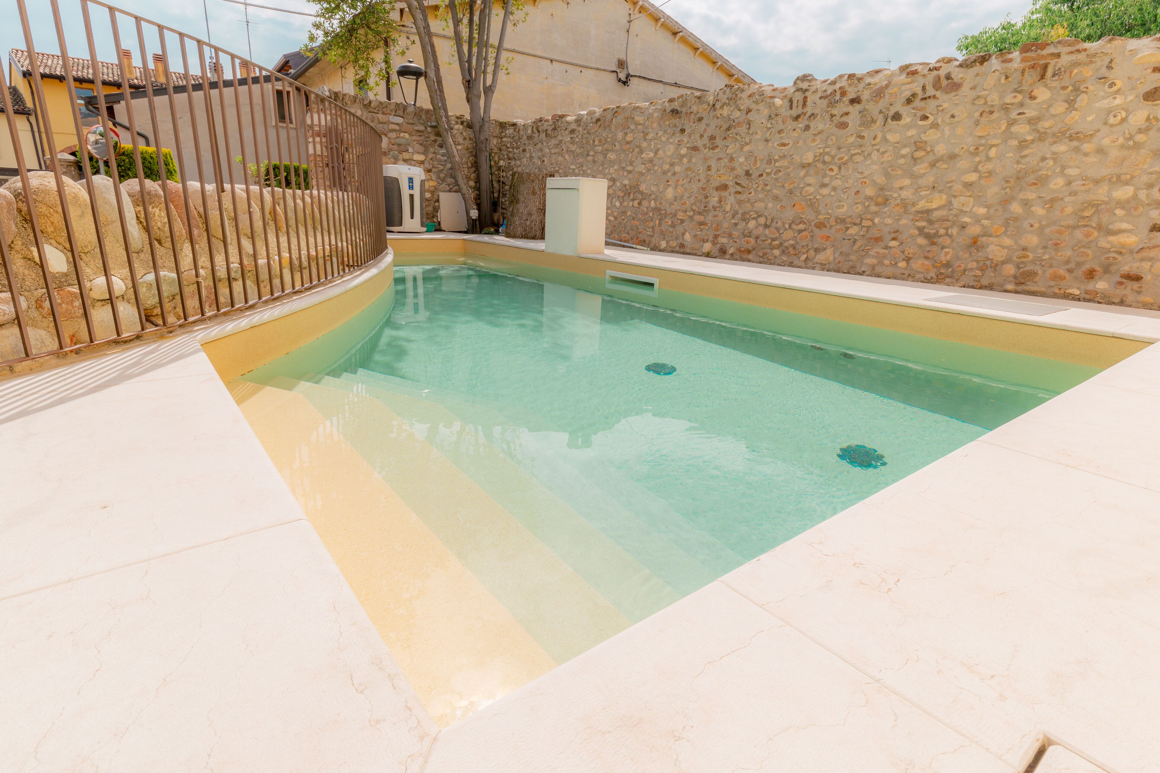 A swimming pool with a stone wall and a metal fence.