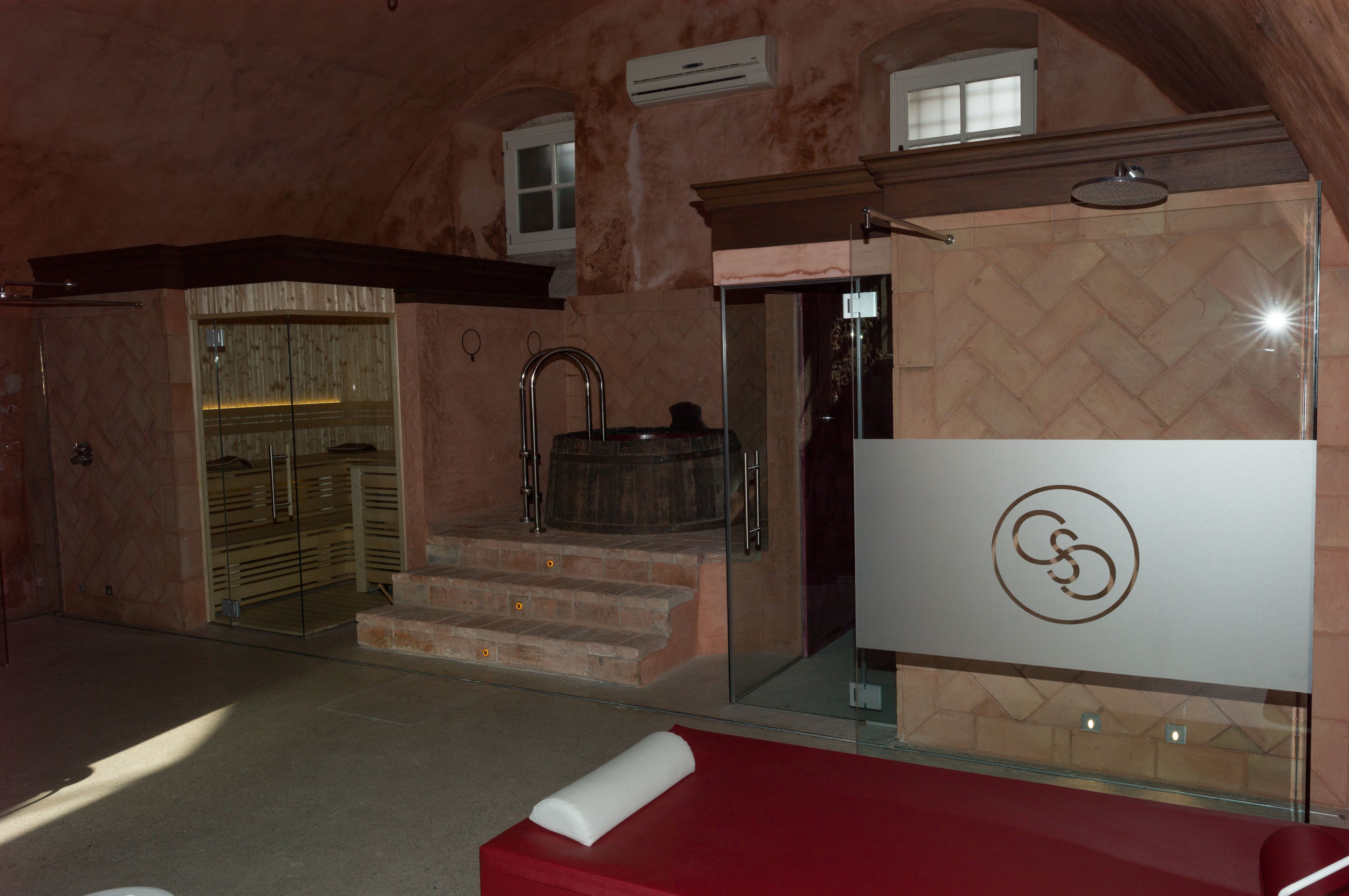 A bathroom with a glass shower enclosure, a wooden bathtub, and a red bench.