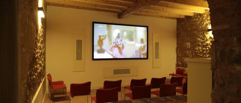 A room with a television mounted on the wall, red chairs arranged in rows, and stone walls.